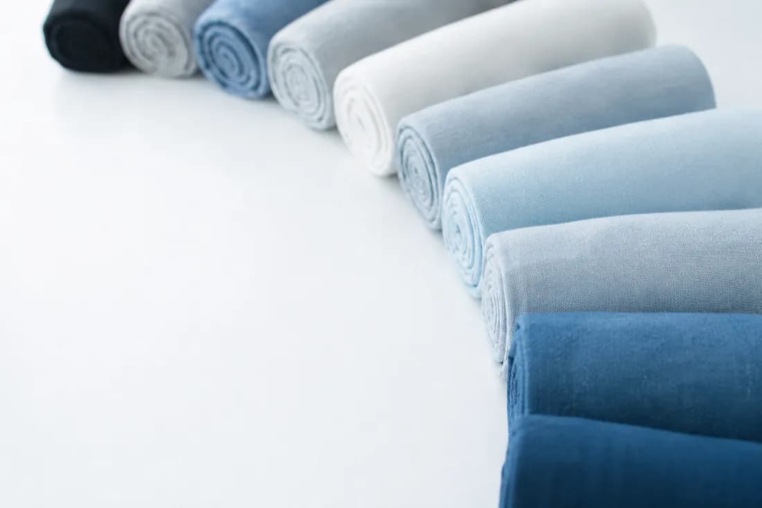A shallow arc of rolled pale fabric cylinders receding into soft focus on a cold white surface.