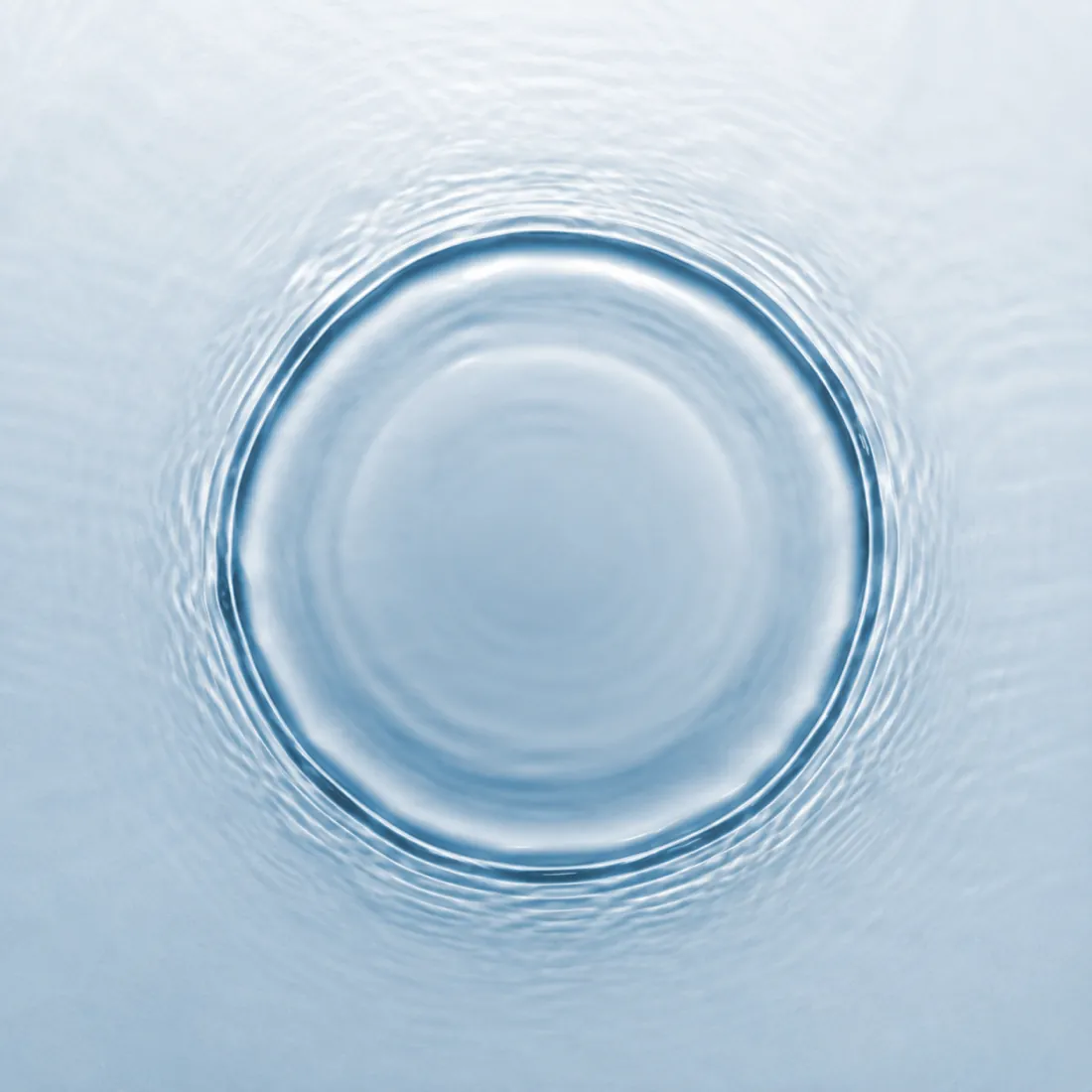 A single circular ripple spreading across still pale water, seen from directly above.