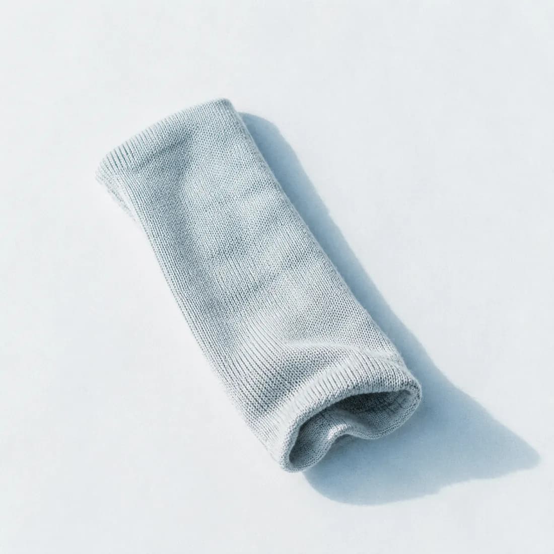 A single knitted tube of pale fabric laid flat on cold white paper.