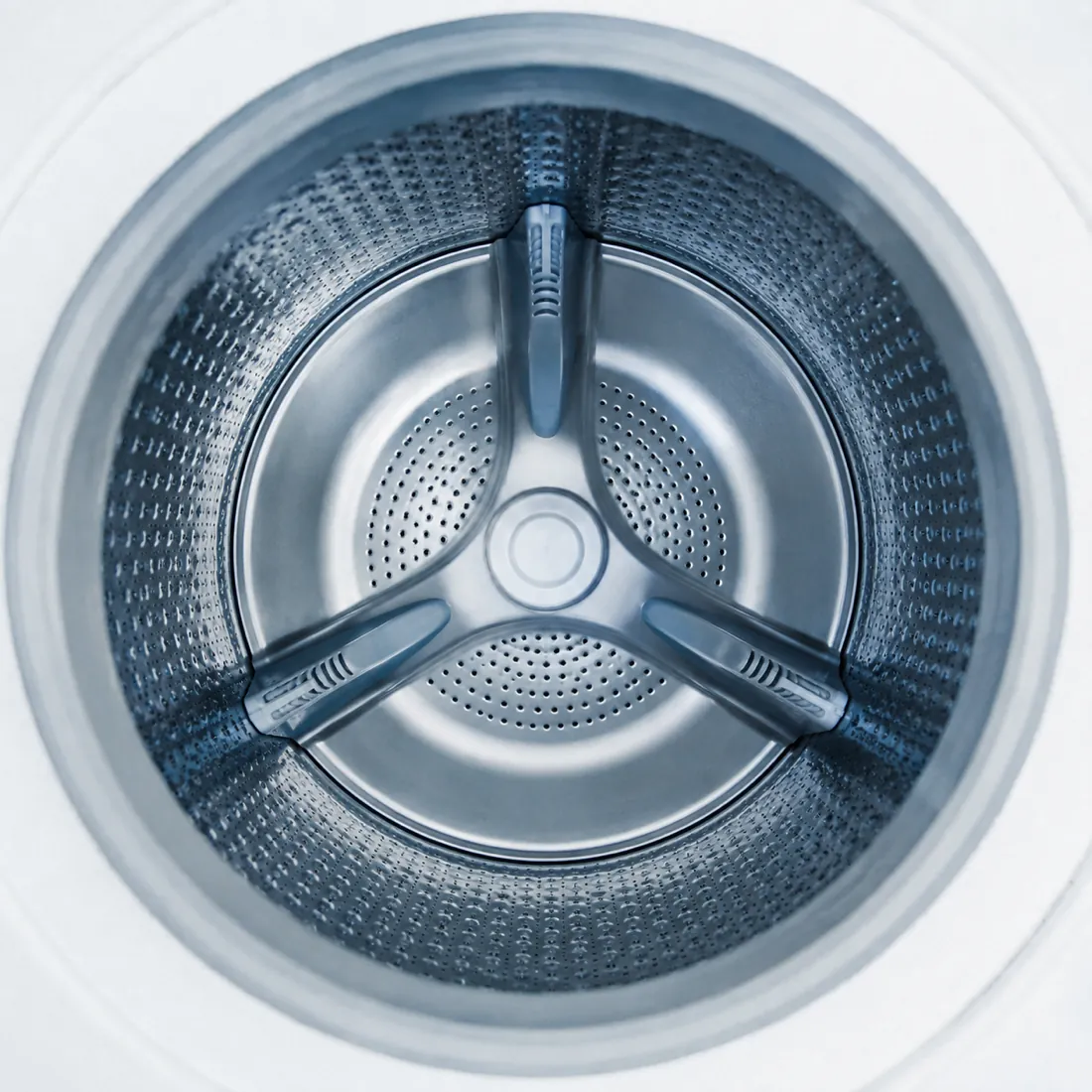 The interior of an empty washing machine drum seen straight on, three paddles forming a triradial pattern.