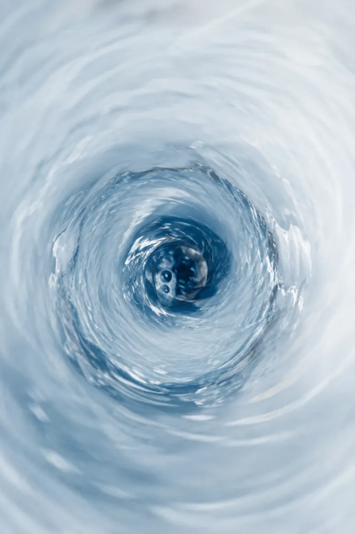 Pale blue water draining in a slow spiral seen from above, concentric motion blur.